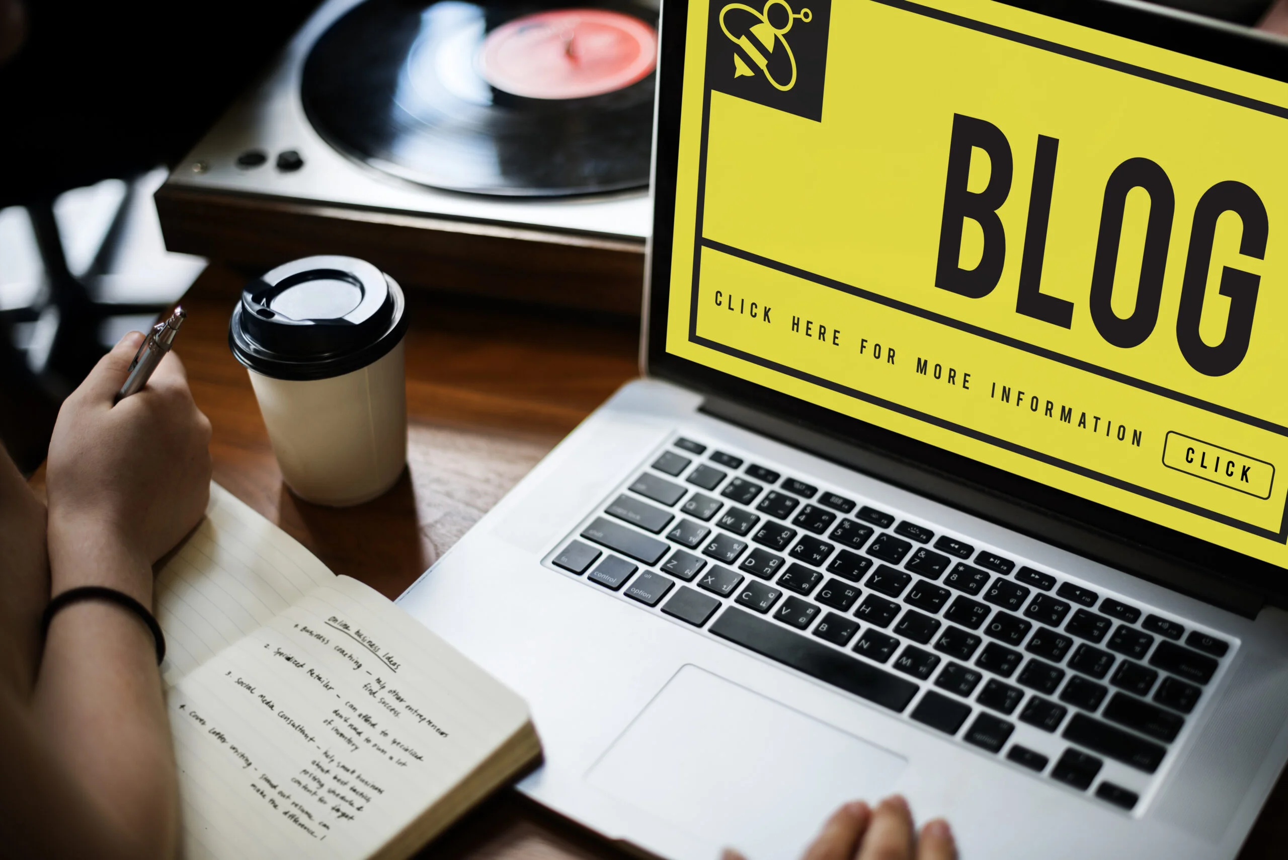 Person planning blog content on a laptop with the word 'BLOG' displayed on screen, representing content writing services, with a notebook, coffee cup, and vinyl record player on the desk